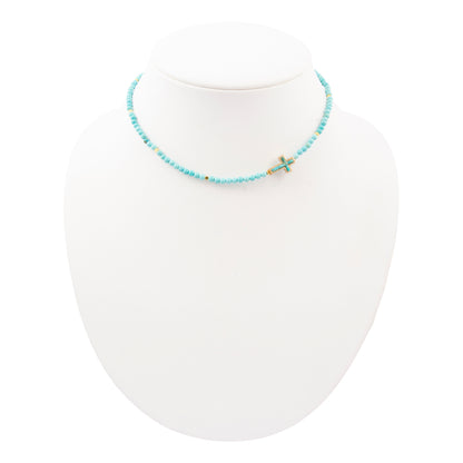 Necklace with turquoise beads and a small cross on a white mannequin.