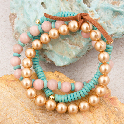 Set of beaded bracelets with gold, pink, and turquoise beads on a textured surface.