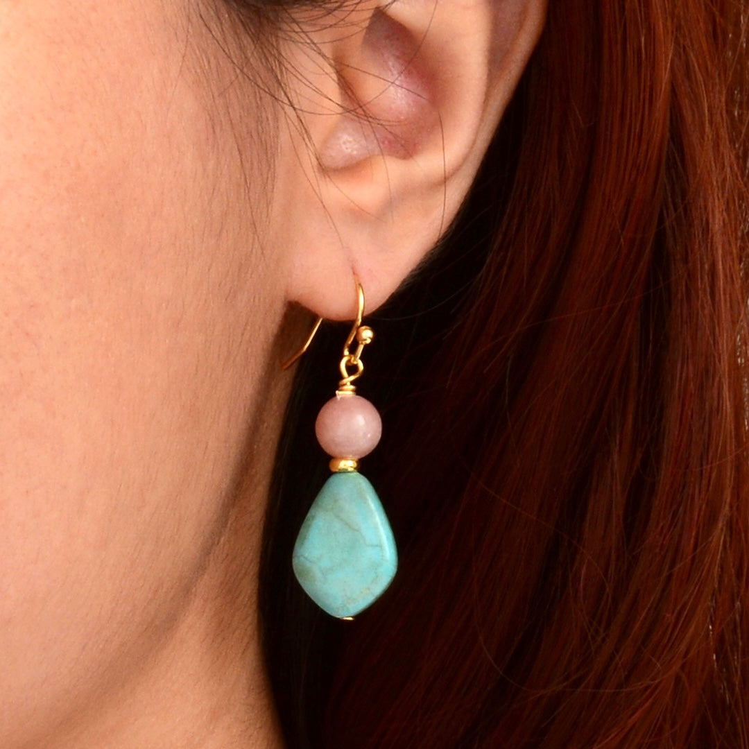 Close-up of an ear wearing a gold earring with a turquoise stone and pink bead.