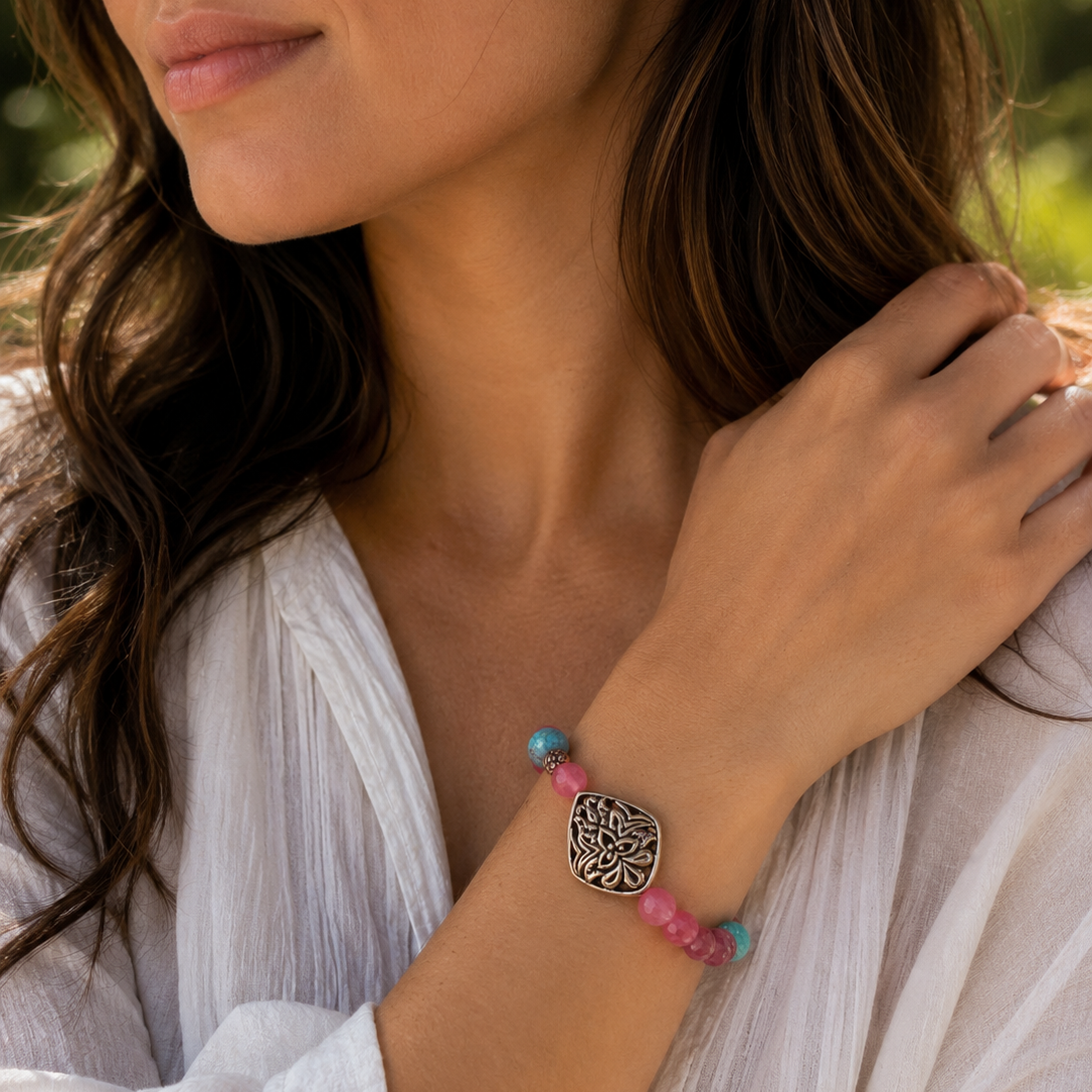 A close-up lifestyle shot of a woman wearing a bohemian-style beaded bracelet on her wrist. The bracelet features pink and turquoise beads with a central oval silver-toned metal charm containing a tree of life design.