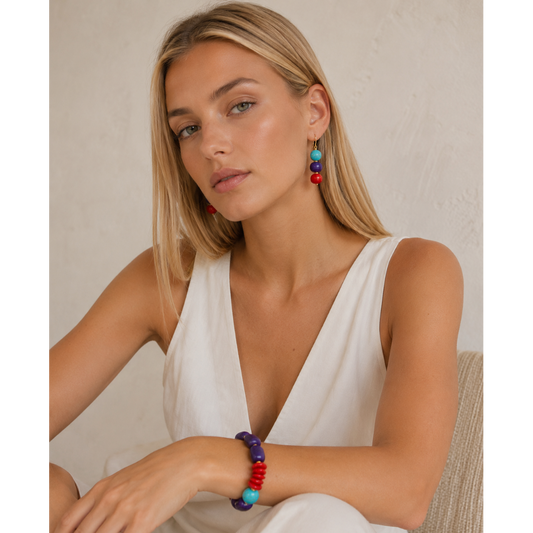Woman wearing colorful earrings and a bracelet against a neutral background