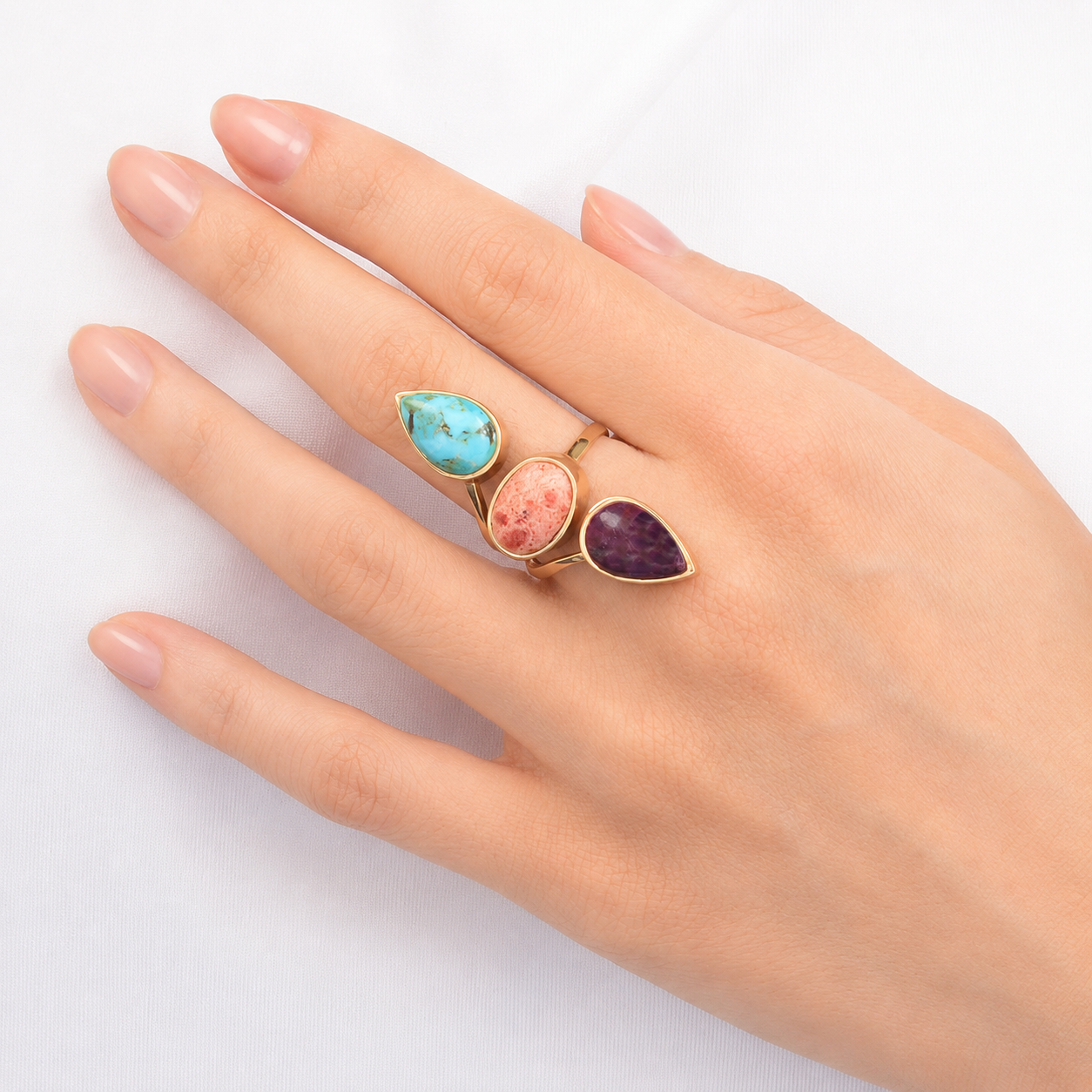 Hand wearing three colorful gemstone rings on a white background