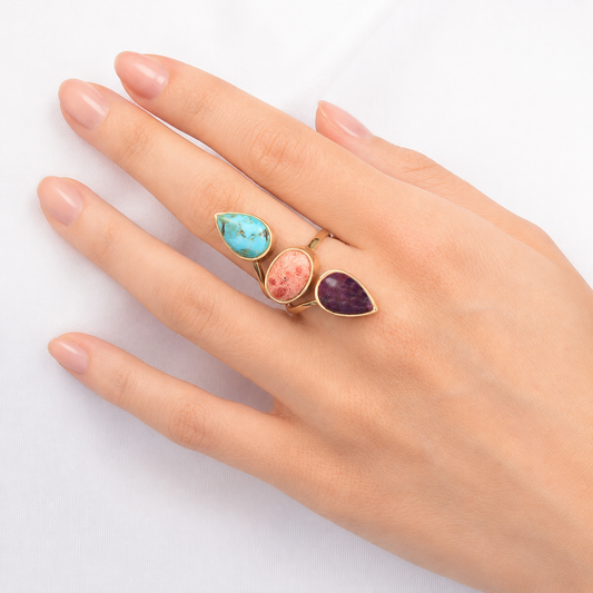 Hand wearing three colorful gemstone rings on a white background