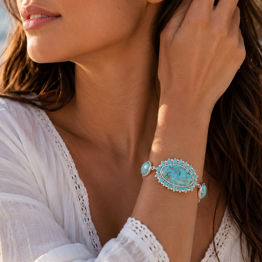 A woman wearing a turquoise and silver cuff bracelet, photographed outdoors near the beach with her hand touching her hair.