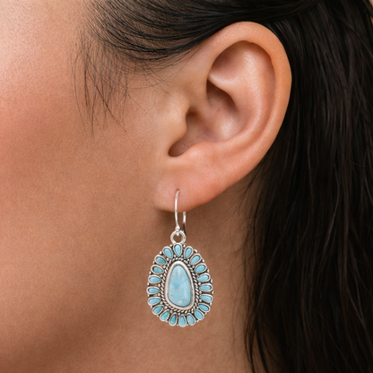Close-up of an ear wearing a turquoise teardrop earring with a dark background