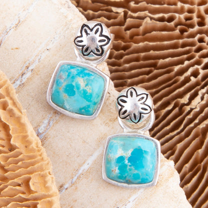 Silver earrings with turquoise stones on a textured stone surface