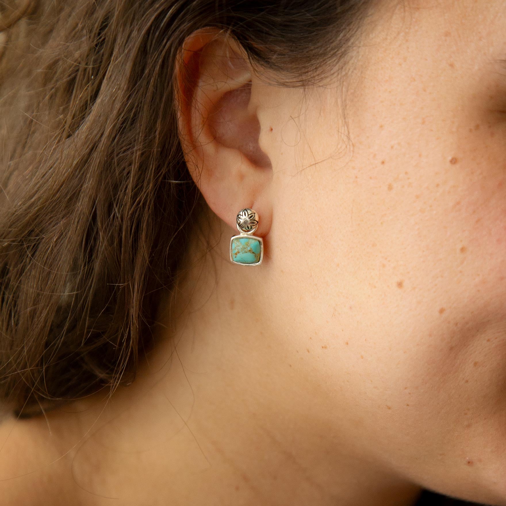 Close-up of a person wearing a turquoise earring with gold accents.