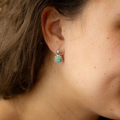 Close-up of a person wearing a turquoise earring with gold accents.