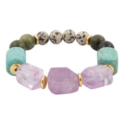 A beaded stretch bracelet featuring large faceted lavender amethyst beads, turquoise-colored jasper beads, green stone beads, and speckled beige-and-black agate beads, separated by small gold spacer rings, on a plain white background.