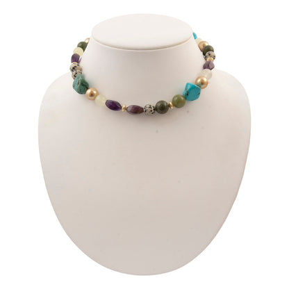 A multi-colored beaded necklace displayed on a white mannequin bust. The necklace features a mix of turquoise, purple, olive green, cream, and metallic gold beads.