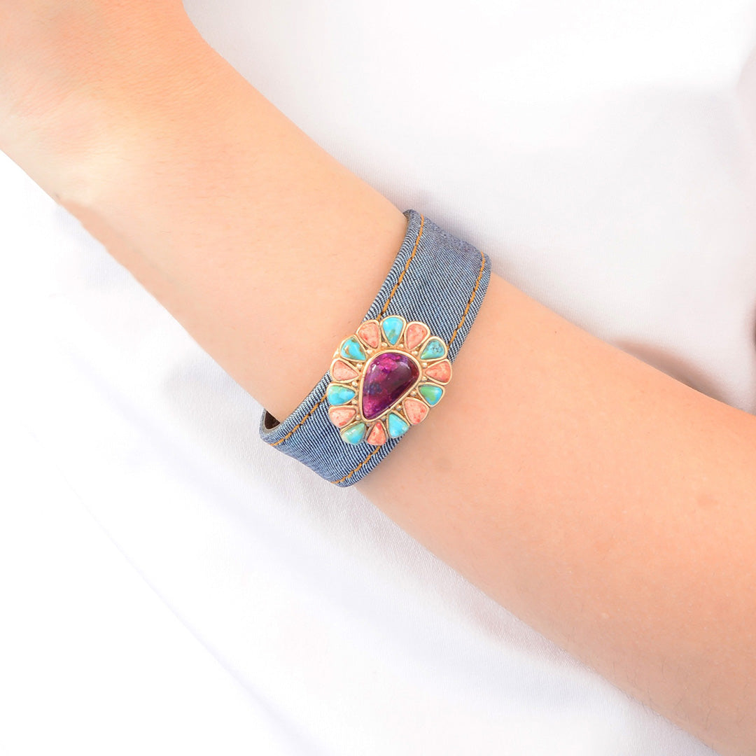 Denim bracelet with a decorative heart-shaped gemstone on a wrist against a white background