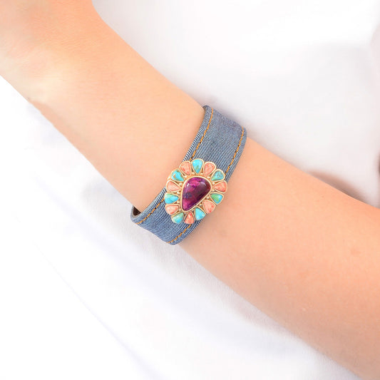 Denim bracelet with a decorative heart-shaped gemstone on a wrist against a white background