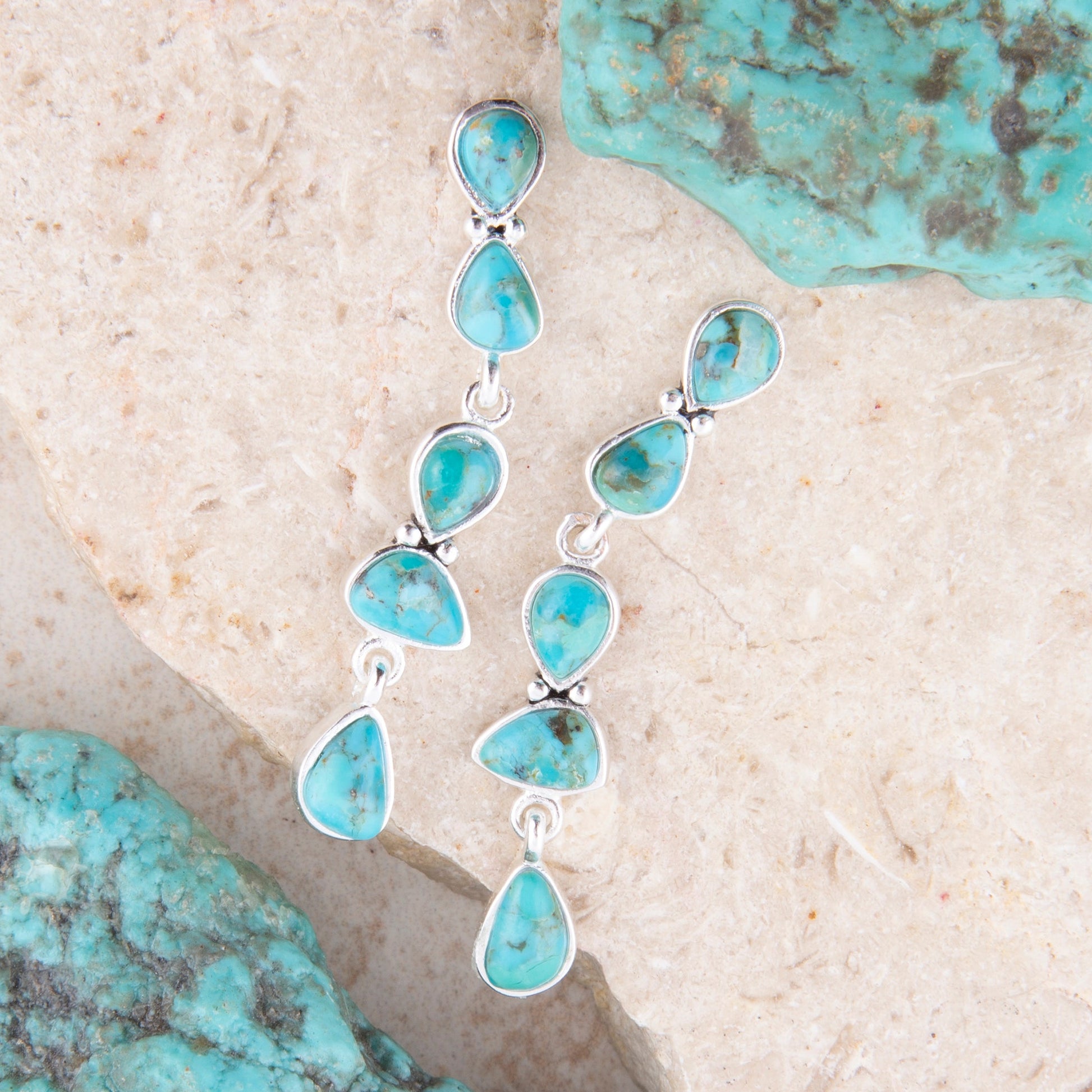 Turquoise teardrop earrings on a textured stone surface