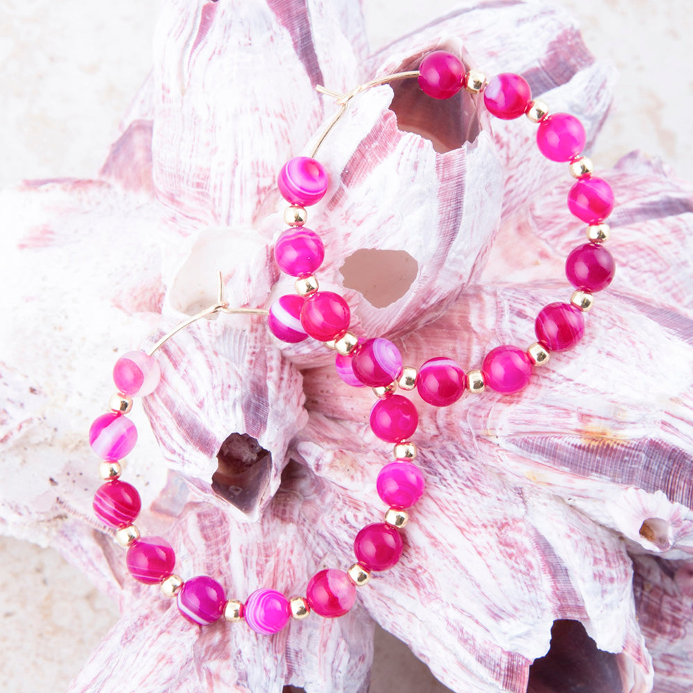 Pink beaded bracelet with gold accents on a seashell background