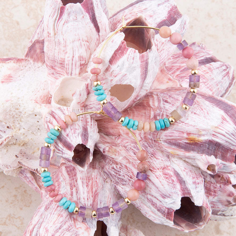 Two beaded bracelets with pastel pink, lavender, turquoise, and cream beads with gold-toned metal, displayed on a large pink seashell.