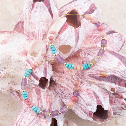 Two beaded bracelets with pastel pink, lavender, turquoise, and cream beads with gold-toned metal, displayed on a large pink seashell.