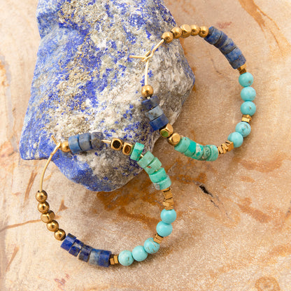 Beaded earrings with blue and green stones on a textured stone surface
