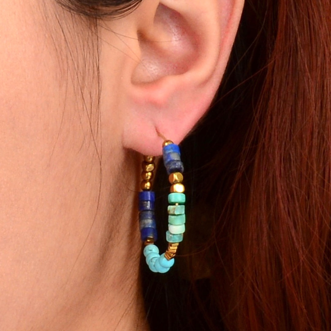 Close-up of an ear wearing colorful beaded hoop earrings with a blurred background.