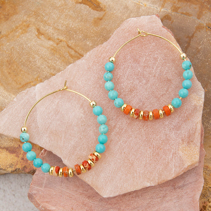 Gold hoop earrings with turquoise and orange beads on a stone surface
