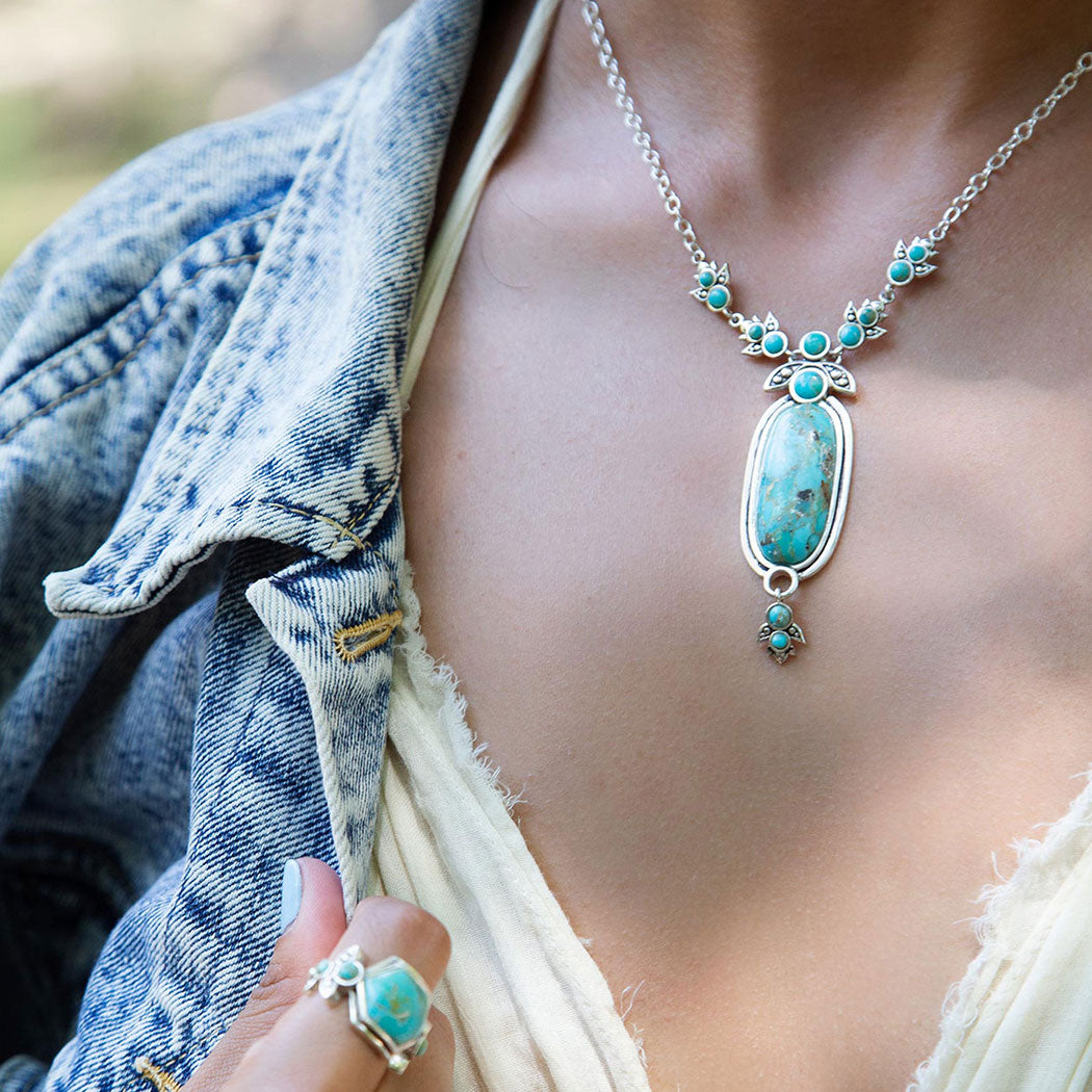 Person wearing a turquoise necklace and ring with a denim jacket