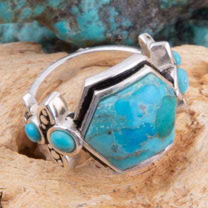 Turquoise and silver ring on a wooden surface with turquoise stones in the background