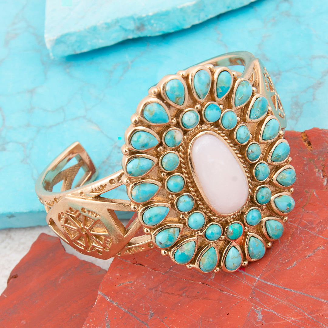 Gold ring with turquoise stones and a central white stone on a textured blue and red background
