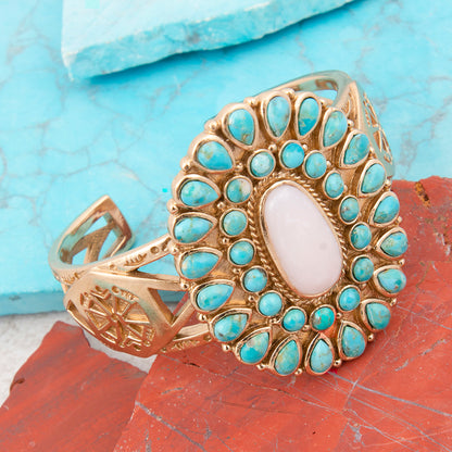 Gold ring with turquoise stones and a central white stone on a textured blue and red background