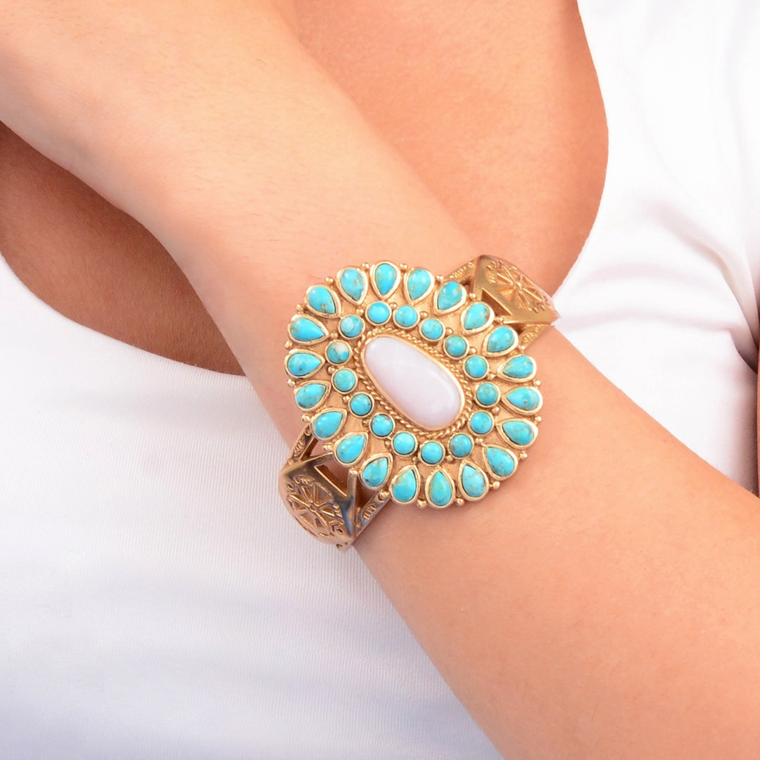 Decorative bracelet with turquoise stones and gold accents on a wrist against a white background