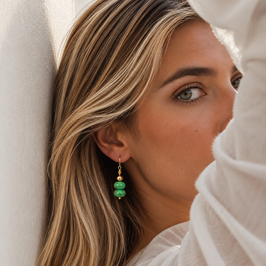 A close-up lifestyle shot of a woman wearing a single drop earring with three stacked green beads and a gold fishhook wire.