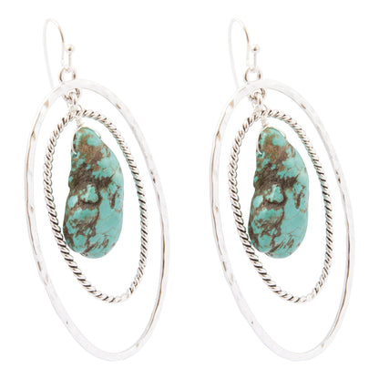 A pair of silver-toned double-ring hoop earrings with a textured, hammered finish and a central turquoise stone featuring brown matrix veining, shown on a plain white background.