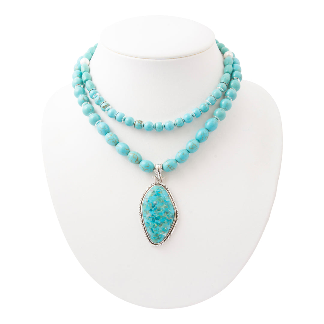 A double-strand turquoise beaded necklace with a large teardrop-shaped turquoise pendant in a silver bezel setting, displayed on a white mannequin bust.