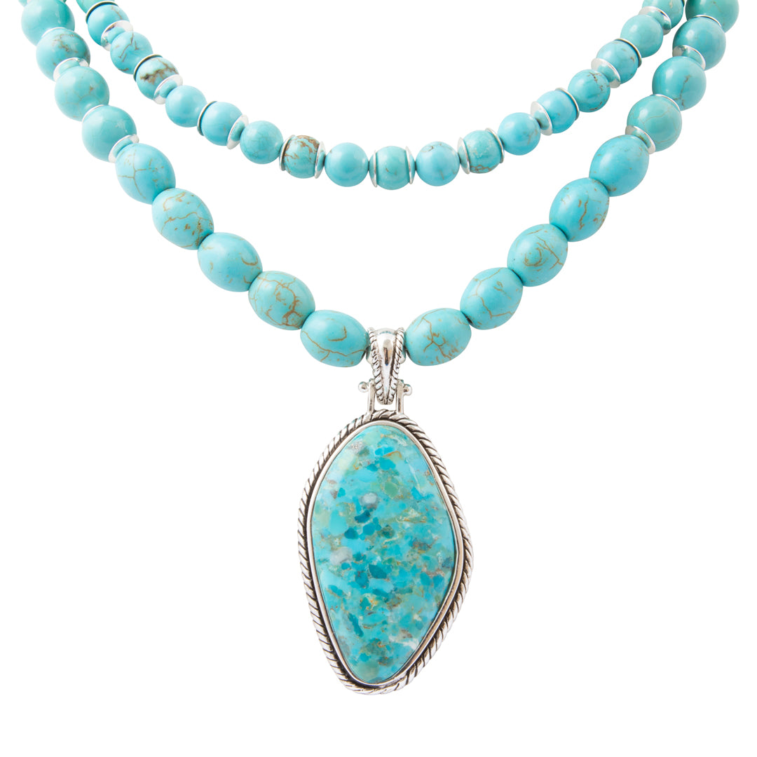 A double-strand turquoise beaded necklace with a large teardrop-shaped turquoise stone pendant in a silver-toned bezel setting, shown against a plain white background.