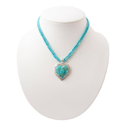A turquoise beaded necklace with a heart-shaped turquoise pendant in a silver frame, displayed on a white mannequin bust against a white background.