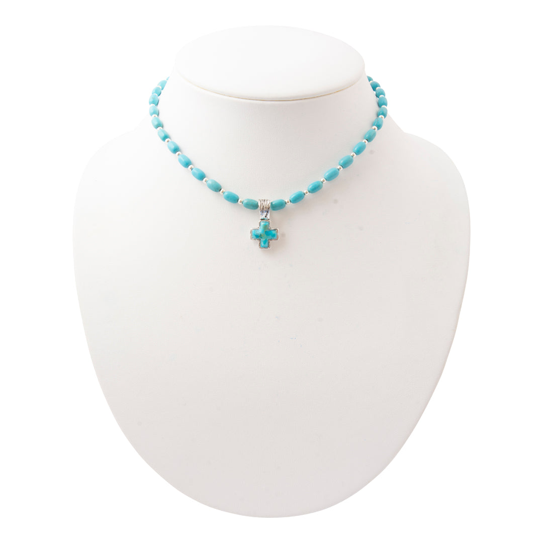 A turquoise beaded necklace with a matching cross pendant on a white display bust.