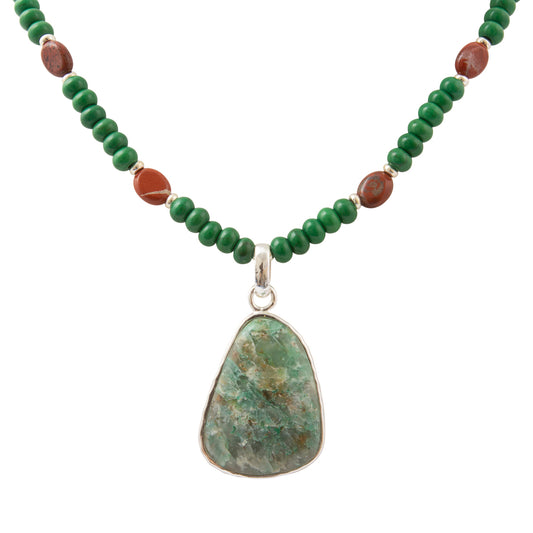 A beaded necklace featuring green round beads, small reddish-brown accent beads, and a large irregular green stone pendant in a silver bezel setting, shown against a plain white background.