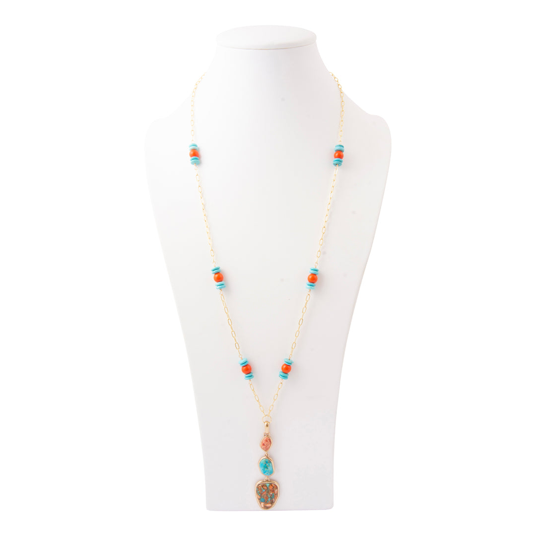 A long gold-tone chain necklace with turquoise and coral beads, displayed on a white mannequin bust against a white background.