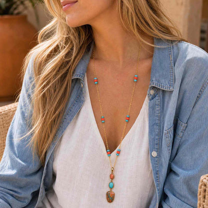 A woman wearing a long gold chain necklace with turquoise and coral beads, styled with a white top and an open light blue denim shirt.
