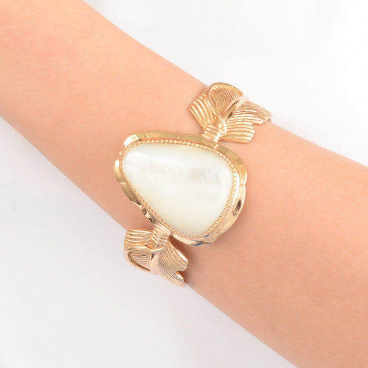 Gold bracelet with a heart-shaped white stone on a wrist against a light background