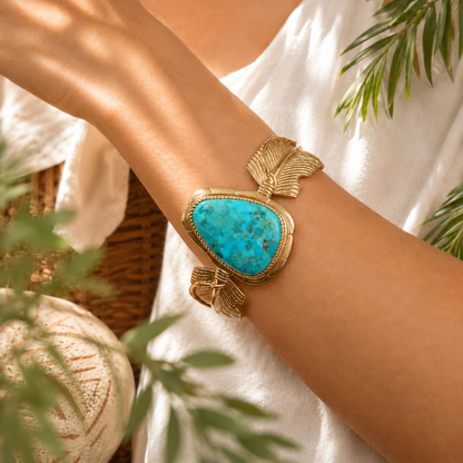 Gold bracelet with a blue stone on a wrist, surrounded by greenery