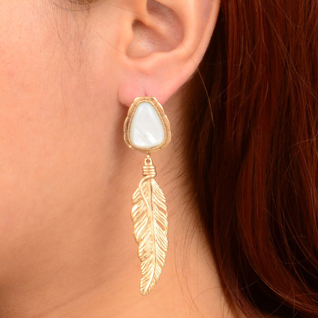 Gold feather earring with a white stone on an ear