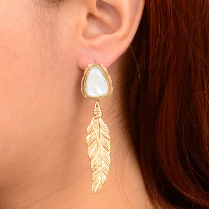 Gold feather earring with a white stone on an ear