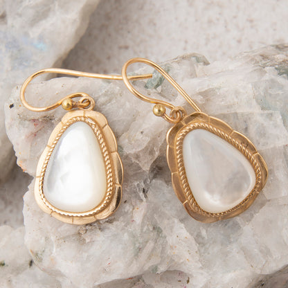 Gold earrings with white stones on a textured stone background