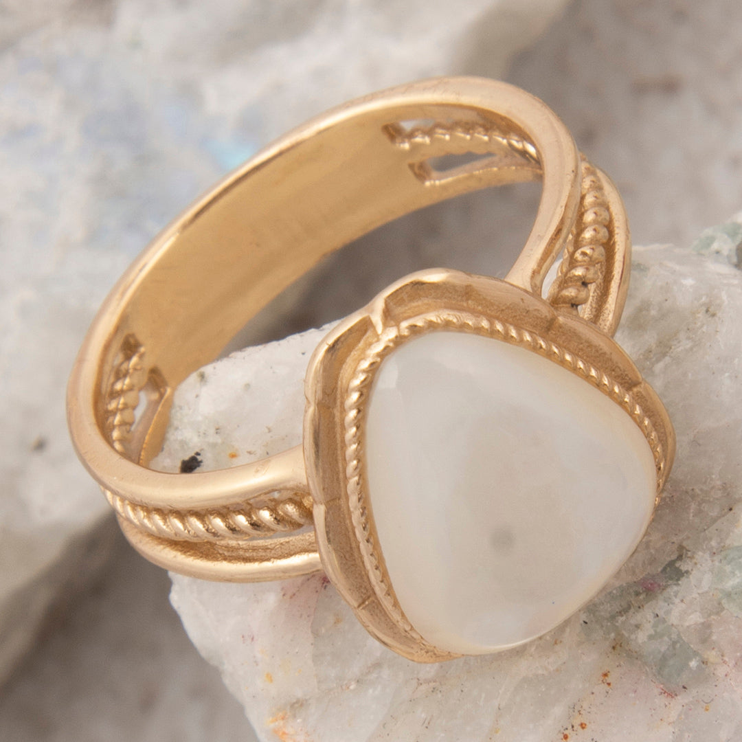 Gold ring with a white stone on a textured surface
