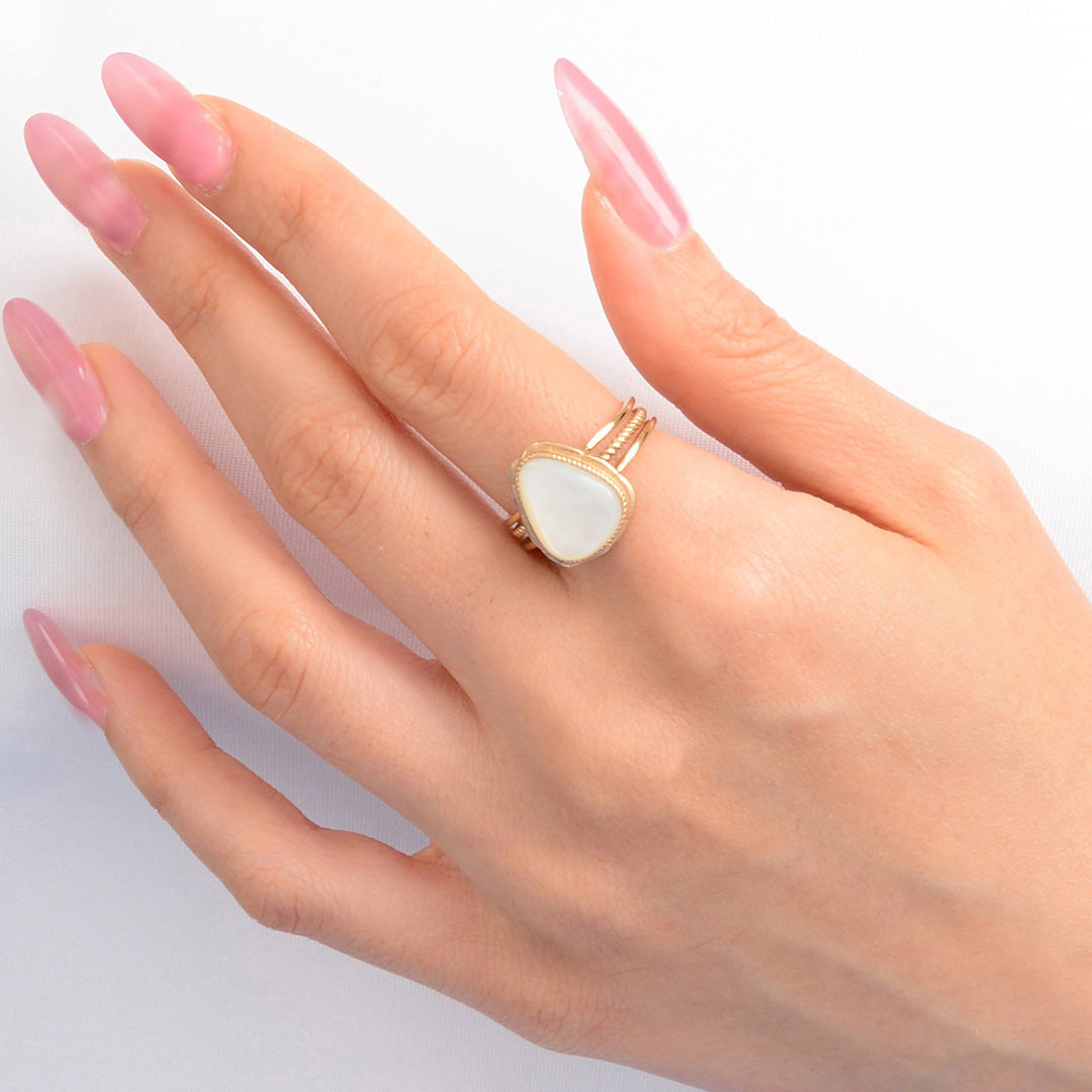 Hand wearing a gold ring with a white stone on a light background