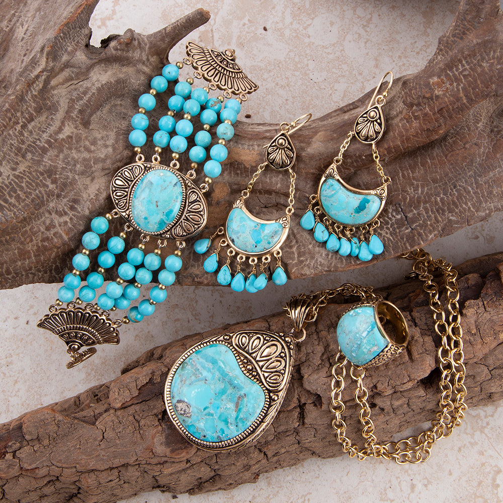 A jewelry set featuring turquoise-blue stone elements and ornate antique gold-toned metalwork, arranged on textured wood branches. The set includes a beaded bracelet, dangling earrings, a pendant necklace, and a ring.