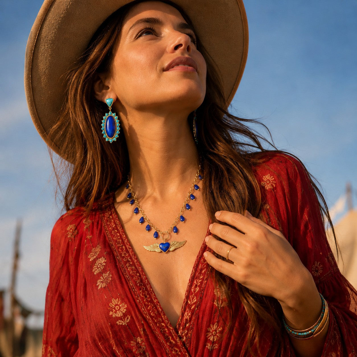 Woman wearing a red dress, brown hat, and blue jewelry against a clear sky.