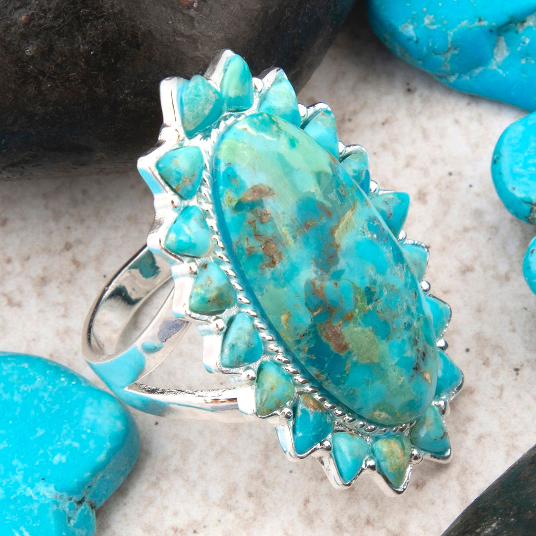 Turquoise stone ring with silver setting on a textured surface with turquoise stones.