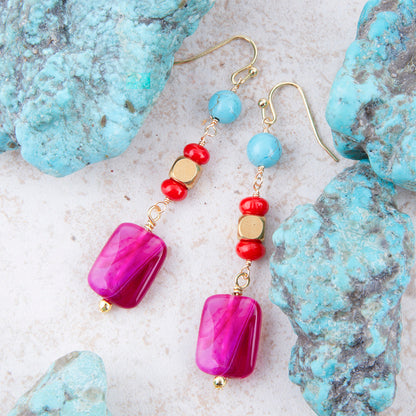 Colorful beaded earrings on a textured surface with turquoise stones.