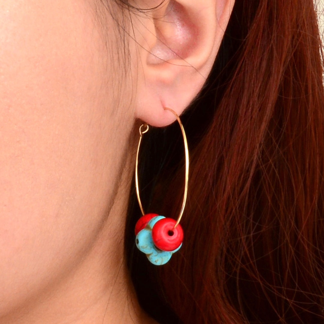 Close-up of an ear wearing a gold hoop earring with red and blue beads.