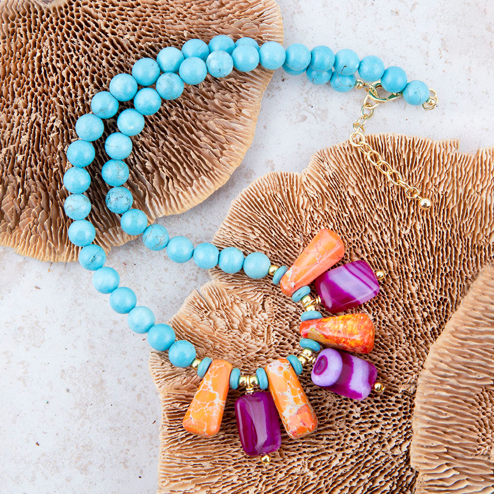 Necklace with blue beads and colorful stone pendants on a textured surface